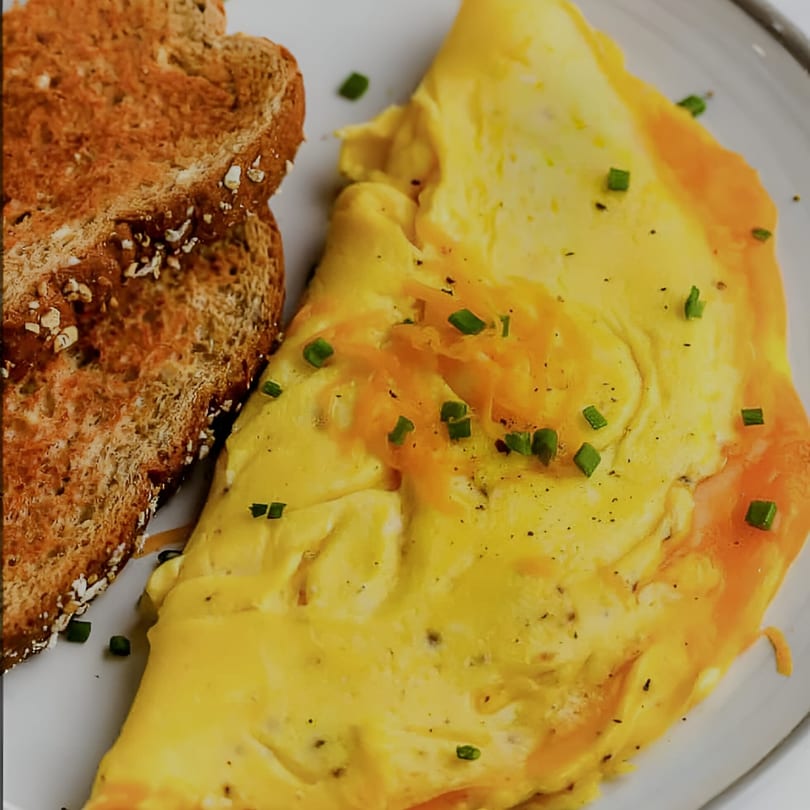 A fluffy yellow omelet topped with cheese and chives, served with two slices of whole wheat toast.